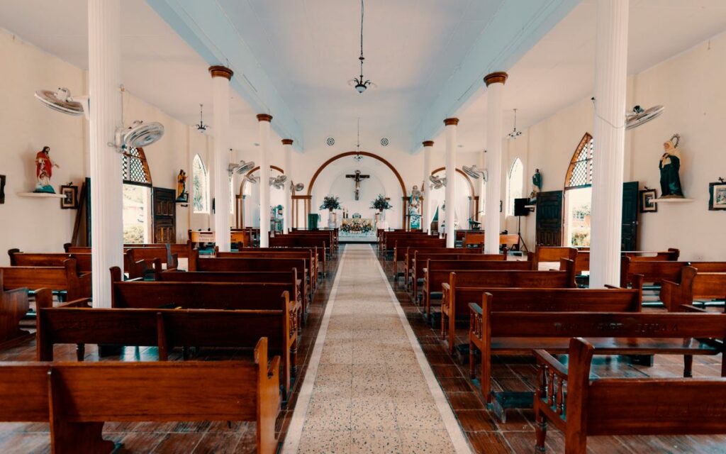 A serene view of the empty interior of a Catholic church, showcasing wooden benches and religious statues.