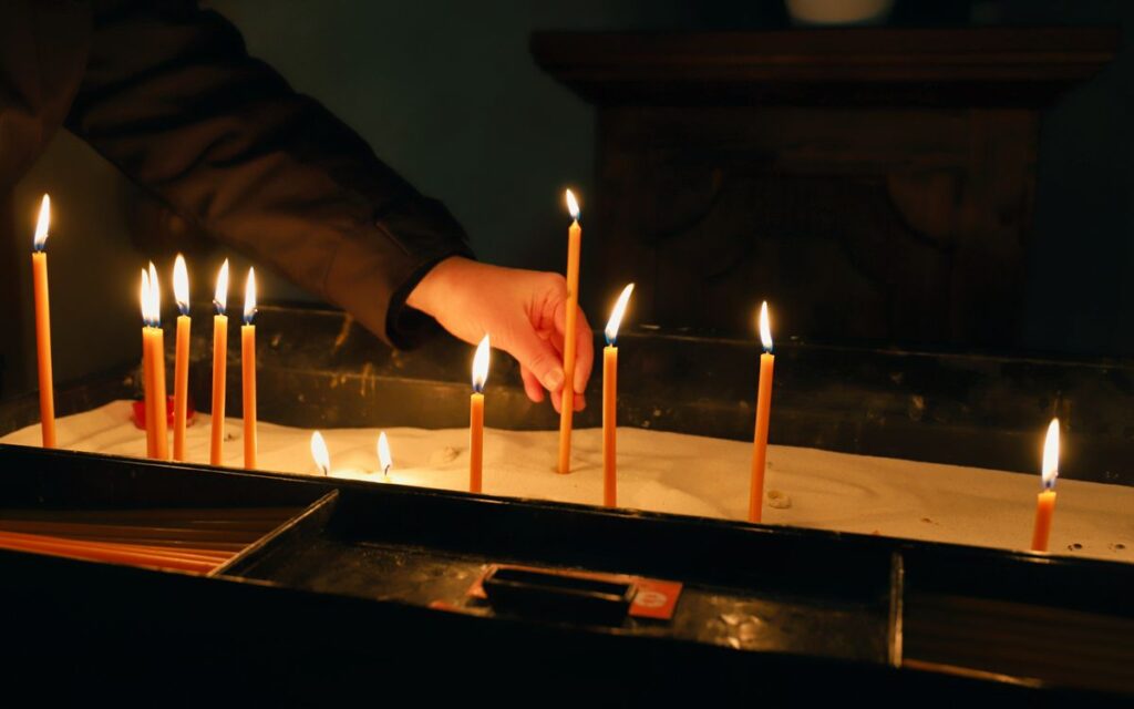 A hand lights slender candles in a church for prayer or reflection.
