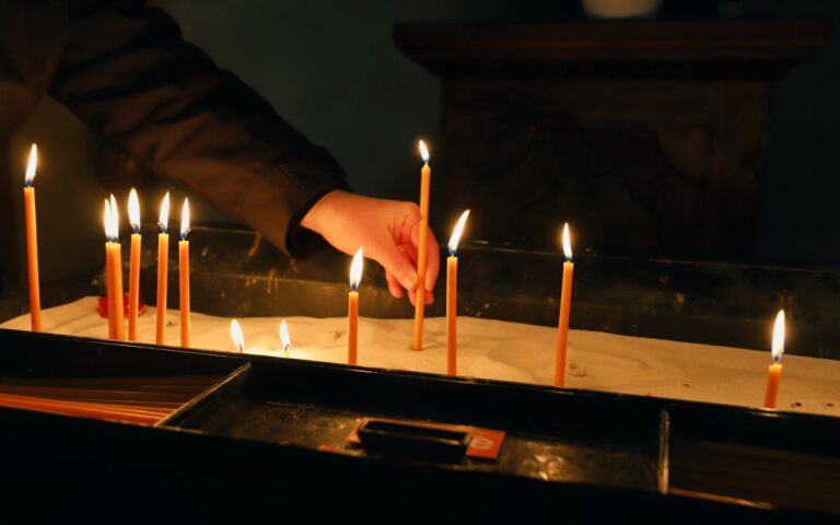 A hand lights slender candles in a church for prayer or reflection.