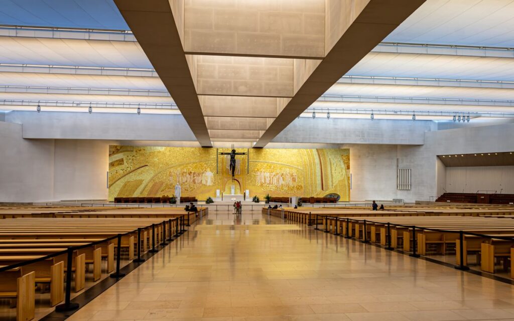 Spacious interior of a modern Catholic church featuring a large golden mural and rows of wooden pews.