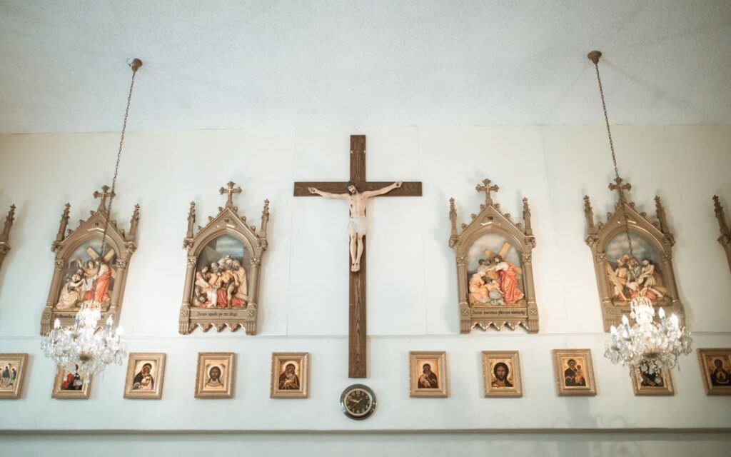 Church interior showcasing wall-mounted crucifix and religious icons under chandeliers.