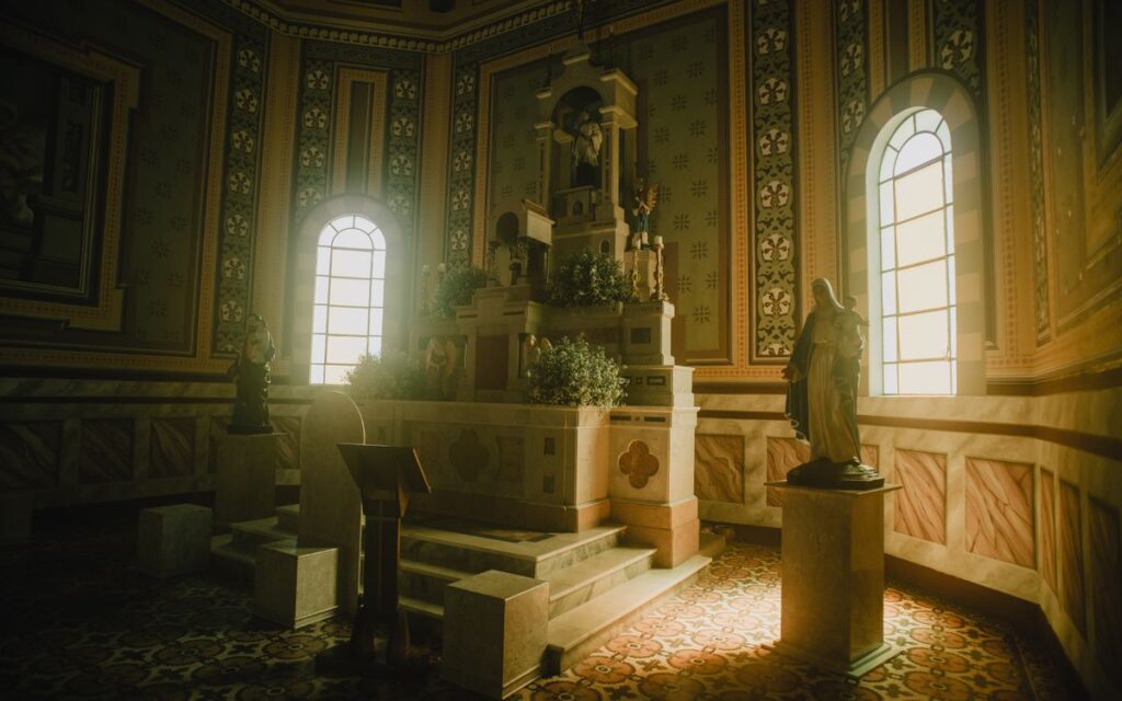 A serene gothic church interior with altar, arched windows, and statues illuminated by warm sunlight.