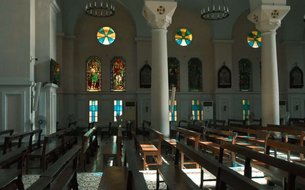 Sunlit church interior with stunning stained glass windows and wooden pews.