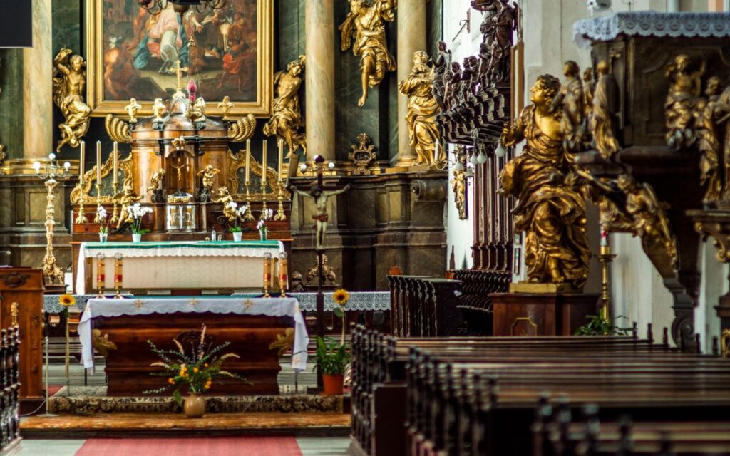 Exquisite baroque church interior featuring a grand altar adorned with gold sculptures and a vibrant painting.