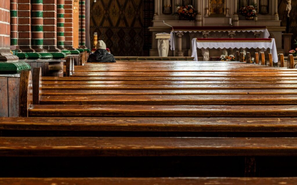 Empty church interior with wooden pews leading to richly decorated altar, warm atmosphere.