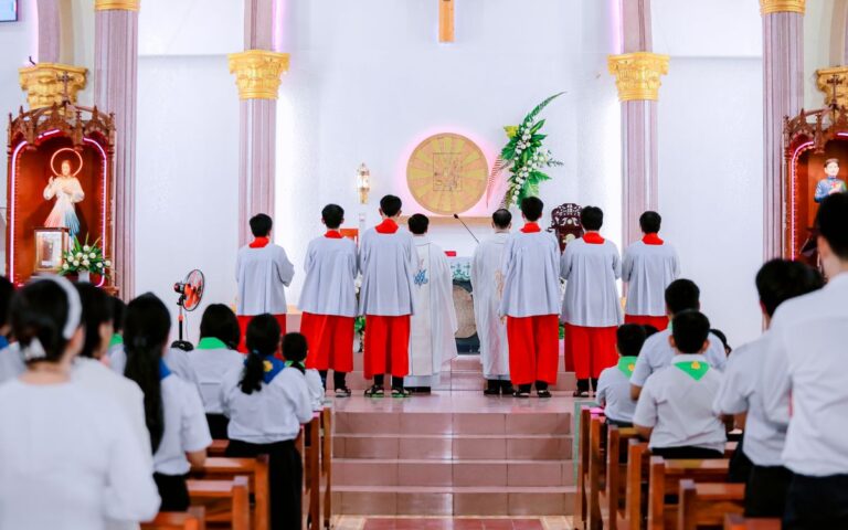 Catholic mass with altar servers and congregation inside a church.