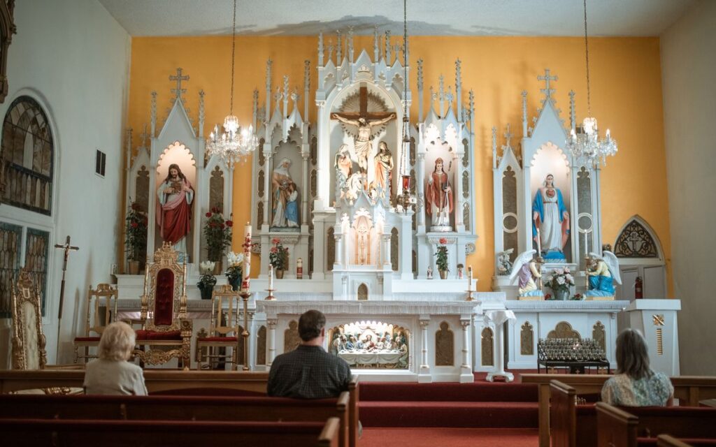 A serene view of a Catholic church altar with attendees in prayer.