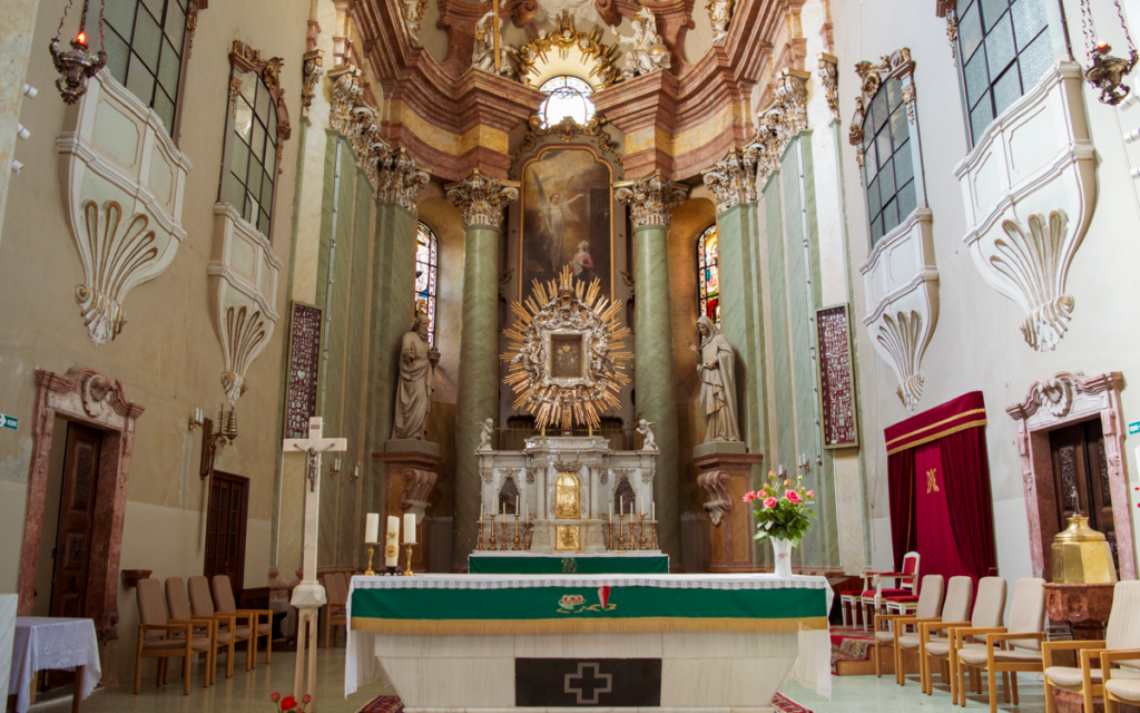 A stunning Baroque church interior featuring an ornate altar surrounded by statues and stained glass.